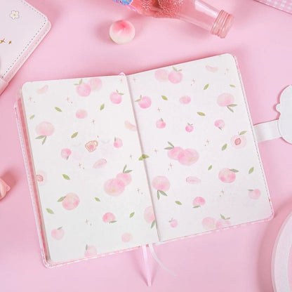 Peach Magnetic Buckle Leather Journal open to a spread of cute peach designs on its pages, surrounded by kawaii pink stationery and decor.