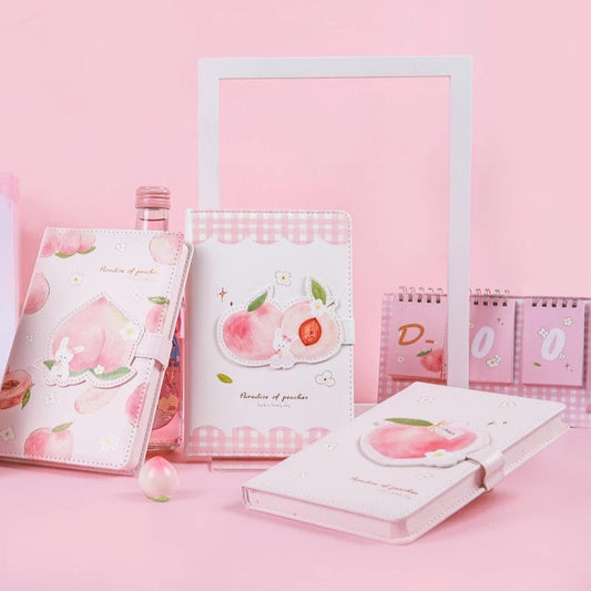 Peach Magnetic Buckle Leather Journal - 228 Pages featuring kawaii peach design, surrounded by additional peach-themed stationery items in a pink aesthetic.