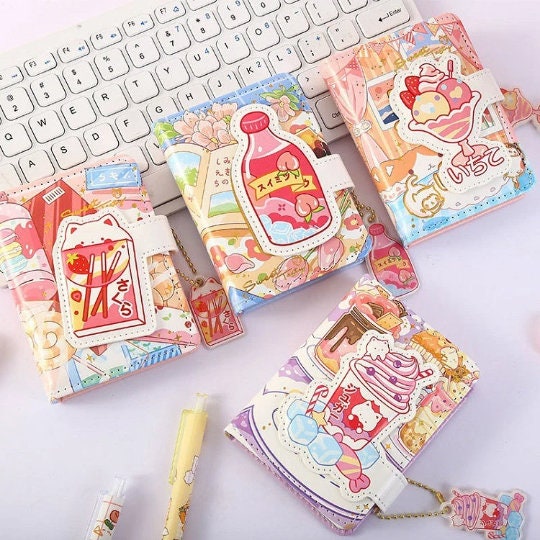 Kawaii A6 leather journals with magnetic buckle and bookmark, featuring cute and colorful designs of sweets and drinks, placed on a white keyboard background.