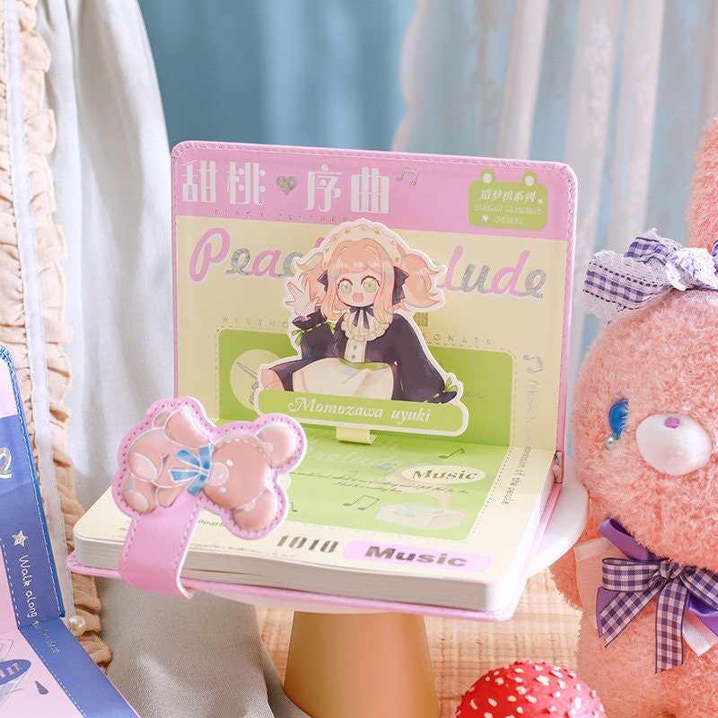 Peach Prelude Leather Journal with Magnetic Buckle featuring adorable anime-style illustration on display, pink teddy bear design on buckle, and pastel color scheme.