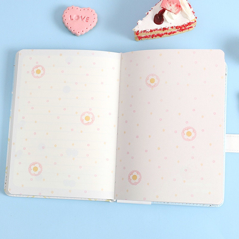 Summer Sundae Leather Journal with Magnetic Buckle featuring kawaii donut-themed interior pages, pastel love-themed decoration, and a slice of cake in the background. Perfect for journaling and note-taking.