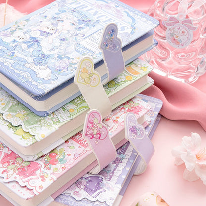 Colorful Princess SAKI A5 Journal with Magnetic Buckle featuring pastel colors and adorable kawaii designs, stacked on a table with pink cloth and floral decoration.