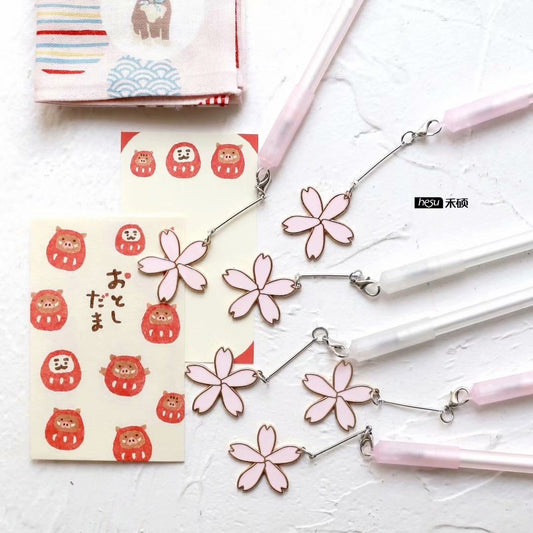 Sakura Kawaii Quick-Dry Black Gel Pen 0.5mm with cute cherry blossom charms, surrounded by Japanese-themed stationery and decorations.