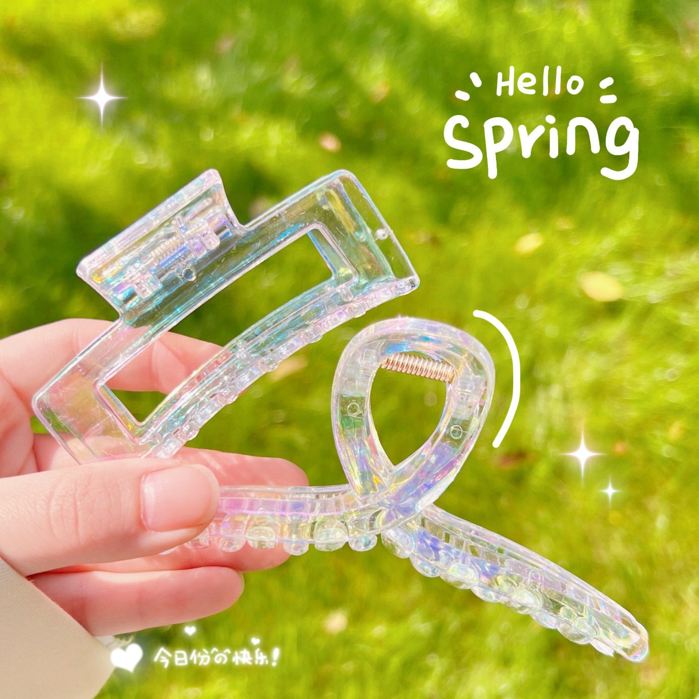 Transparent rainbow acrylic hair claw clip held against a green background with "Hello Spring" text.