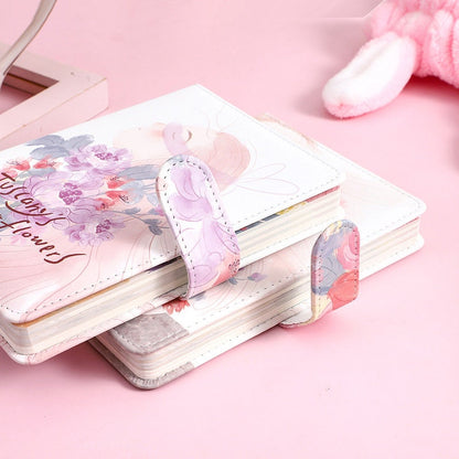 Tuscany's Flowers Leather Journal with Magnetic Buckle, featuring pink floral designs on a white background, displayed on a pastel pink surface.