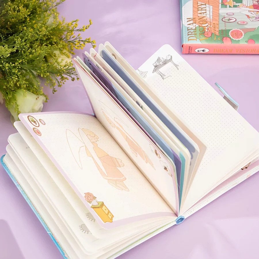 Dream Visionary Magnetic Buckle Leather Journal open to show colorful illustrated pages, surrounded by delicate green flowers on a pastel purple background.