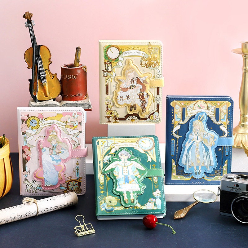 Romantic Dream Leather Journal - Magnetic Buckle A5 Notebook with intricate kawaii designs, featuring multiple illustrated covers in pastel colors, displayed alongside decorative items like a violin, camera, and vintage props.