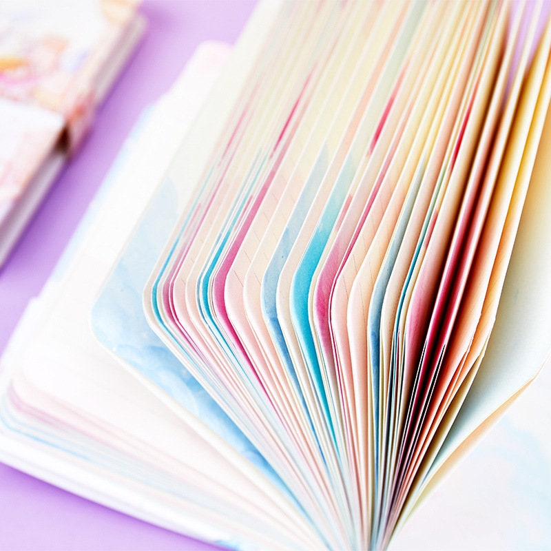 Close-up of an open Magnetic Buckle Leather Journal - Around the Sky Design, showcasing its pastel-colored pages against a purple background. Kawaii stationery.