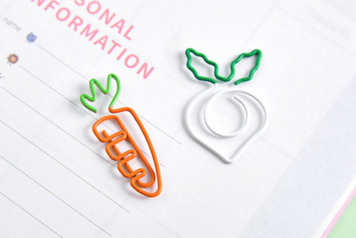 Creative vegetable-shaped paper clips in carrot and turnip designs on a sheet of paper, cute stationery and office supplies