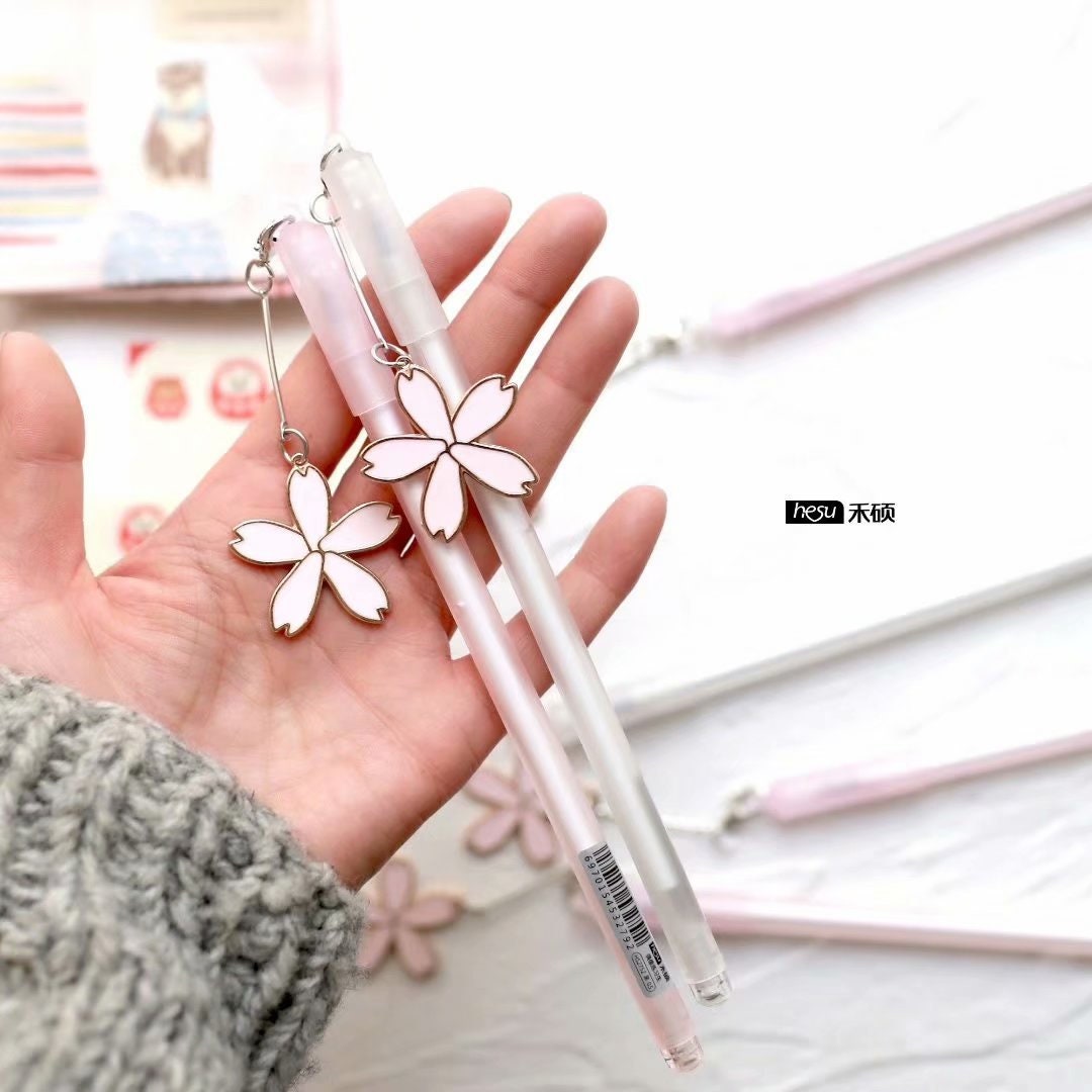 Sakura Kawaii Quick-Dry Black Gel Pen 0.5mm with cute sakura flower charm in hand, pink and white pen design perfect for school and office use