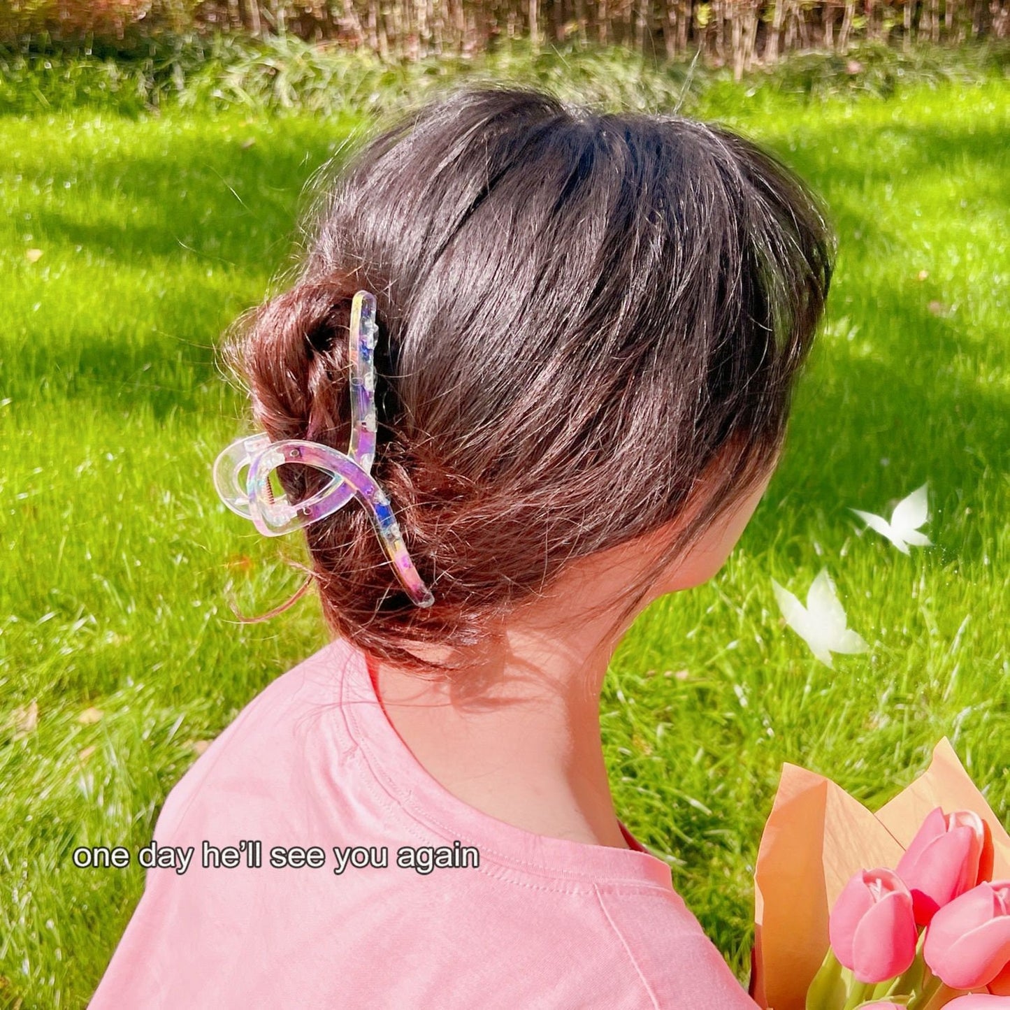 Transparent Rainbow Acrylic Hair Claw Clip holding brunette hair in a stylish updo; woman wearing pink shirt and holding bouquet of tulips in a grassy outdoor setting.