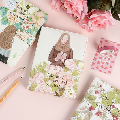 Like Wind Fog Cloud Leather Journal with Magnetic Buckle featuring a whimsical illustration of a girl reading amidst pastel floral designs, surrounded by pink flowers and stationery.