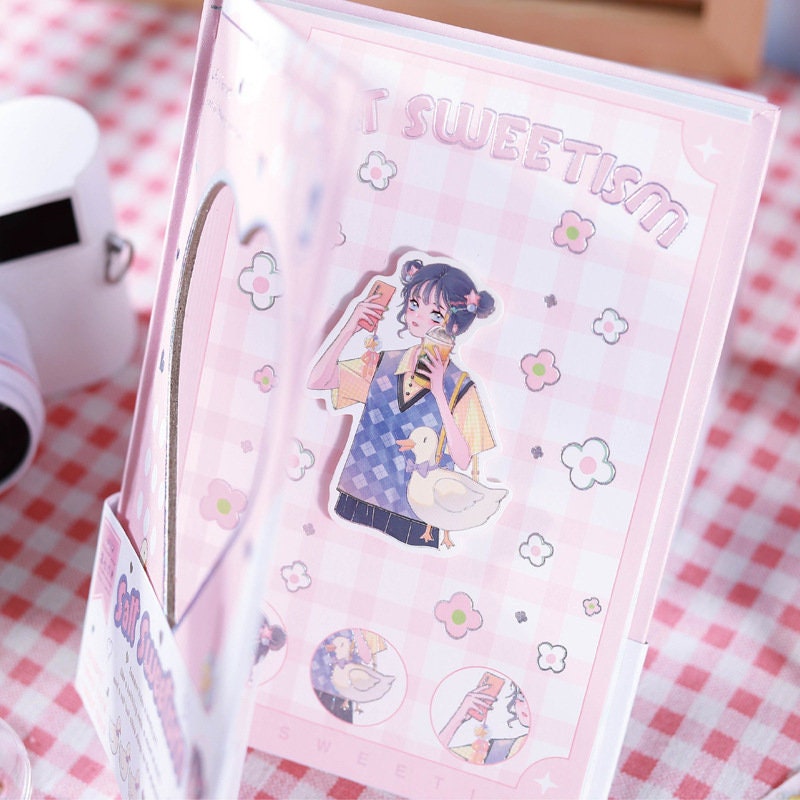 Magnetic Buckle Kawaii Anime Girl Journal featuring a cute anime girl holding a phone with a duck, pink checkered background, floral designs, and "Sweetism" text on the cover.