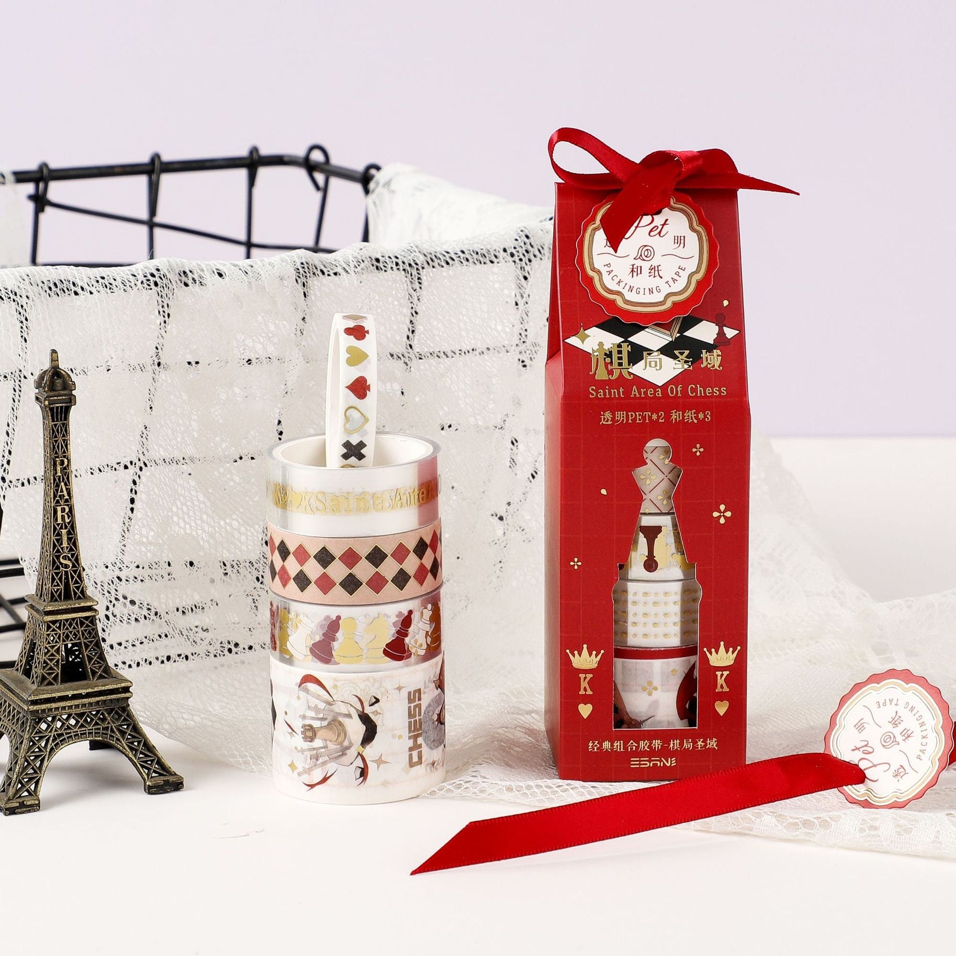 The Queen's Gambit Washi Tape Set - 5 Rolls featuring chess-themed designs; elegant packaging with red and gold details; Eiffel Tower miniature and lace fabric background. Perfect for scrapbooking and decorating.