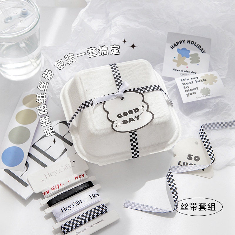 Gift wrapping ribbon set with stickers and cards, featuring black and white checkered ribbon, "Good Day" tag, "Happy Holiday" and "It's my best luck to meet you" cards, and decorative stickers.