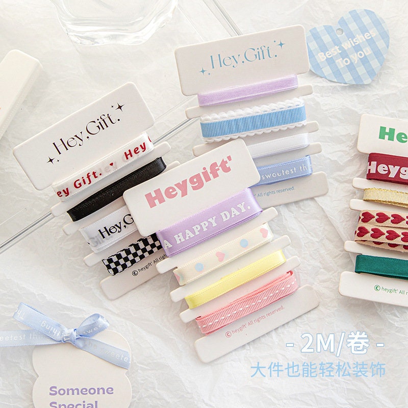 Gift wrapping ribbon set with a variety of colorful designs including "Hey Gift" text, polka dots, hearts, and pastel shades, packaged with coordinating stickers and cards for special occasions.