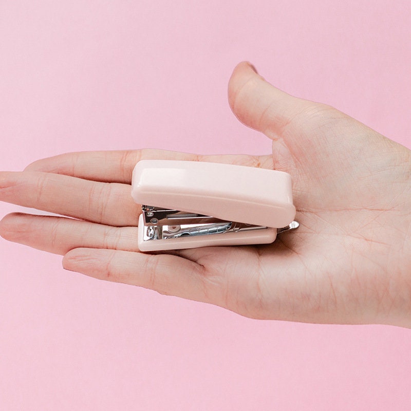 Nature-themed mini stapler in pastel pink, perfect for planners and scrapbooking, displayed on an open palm against a pink background.