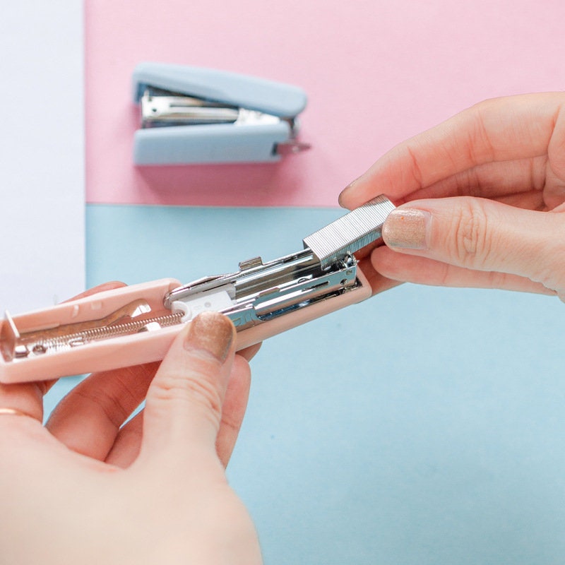 Person loading staples into a nature-themed mini pink stapler for planners and scrapbooking with a light blue stapler in the background.