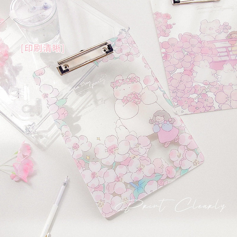 Sakura animal design clipboard in sturdy plastic featuring adorable kawaii-style bear and girl surrounded by pink cherry blossoms, perfect for organizing documents in cute fashion.