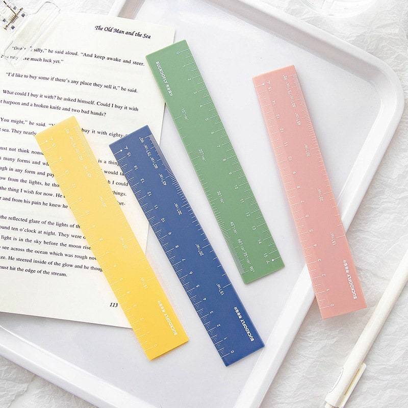 Colorful vegetable-themed decorative paper clips for office or school use, displayed on an open book and a white tray with pastel rulers and a pen.