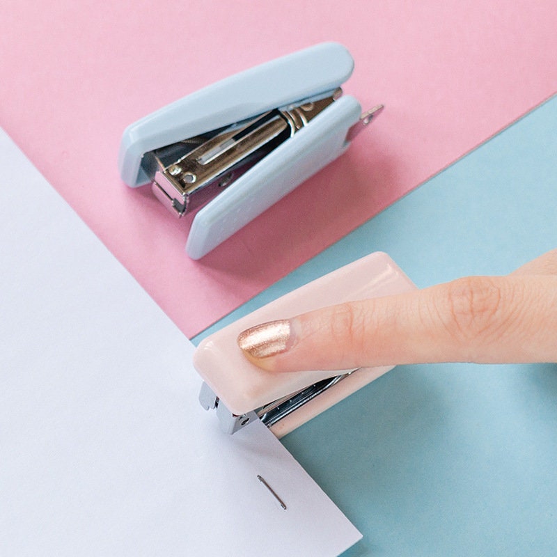 Nature-themed mini stapler in pastel colors for planners and scrapbooking, featuring a person stapling papers with a pink mini stapler and a blue stapler in the background.