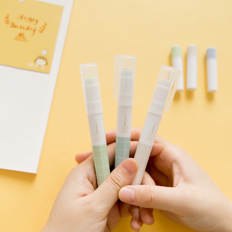 Kawaii Glue Stick for Scrapbooking and Journaling, held in hands with pastel-colored caps, perfect for arts and crafts on yellow background.